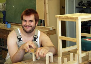 Die Grafik zeigt einen Beschäftigten, welcher an seinen Holzstuhl Feinarbeiten vornimmt.